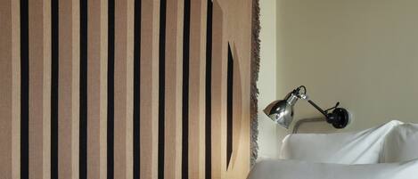 A bed with white linens, a headboard with vertical wooden slats, and a bedside lamp.