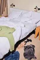 Een bed met witte lakens, een groene deken en een houten nachtkastje.