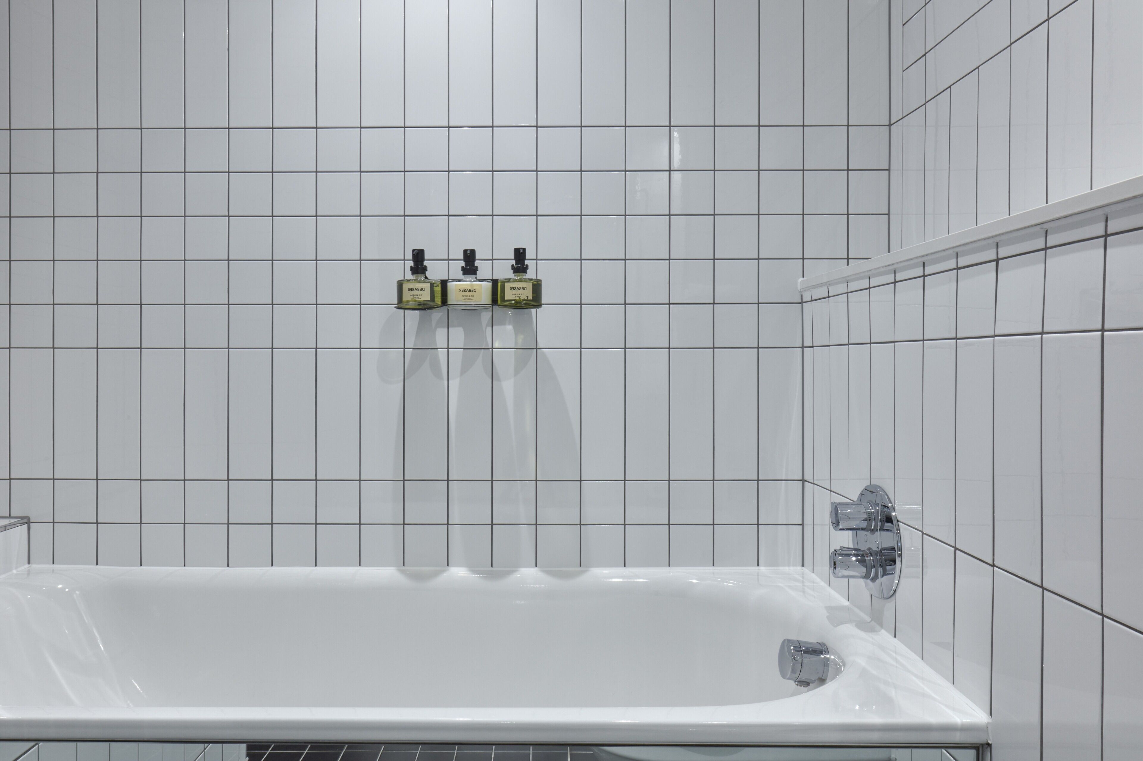 Un baño con una bañera blanca, un grifo de cromo y tres botellas de champú en la pared.