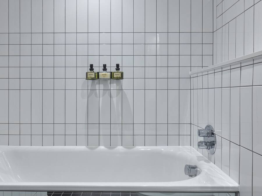 A bathroom with a white bathtub, a chrome faucet, and three bottles of shampoo on the wall.