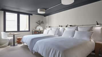 Un dormitorio moderno con dos camas, una mesita, una silla y una ventana que deja entrar luz natural.