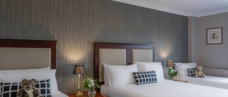 A hotel room with two beds, each with a headboard, a bedside table with a lamp, and a teddy bear.