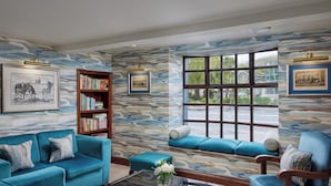Una sala de estar con un sofá azul, una estantería de madera y un ventanal con vistas al verdor.