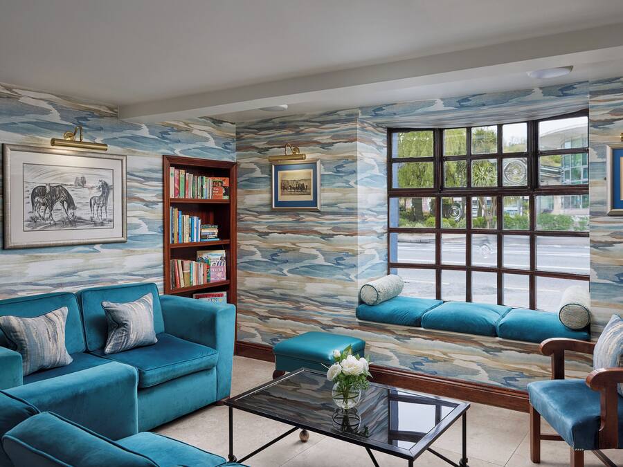 A living room with a blue sofa, a wooden bookshelf, and a window with a view of greenery.
