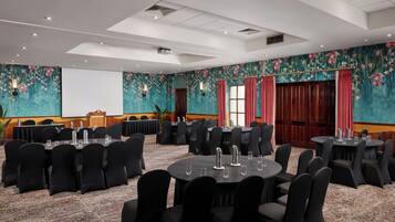 A conference room with round tables and black chairs, a stage with a podium, and floral wall decorations.