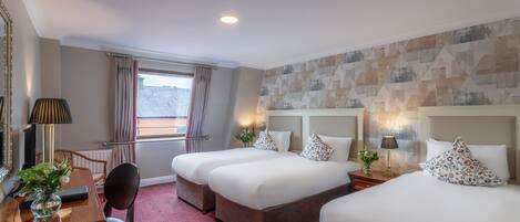 A hotel room with two beds, a desk, a chair, a lamp, and a window with curtains.