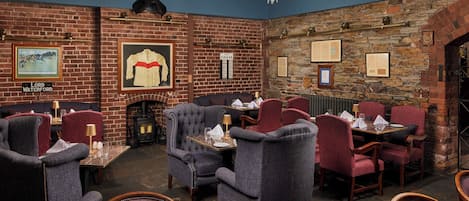 A restaurant with brick walls, framed pictures, and a chandelier. Tables are set with chairs and dining ware.