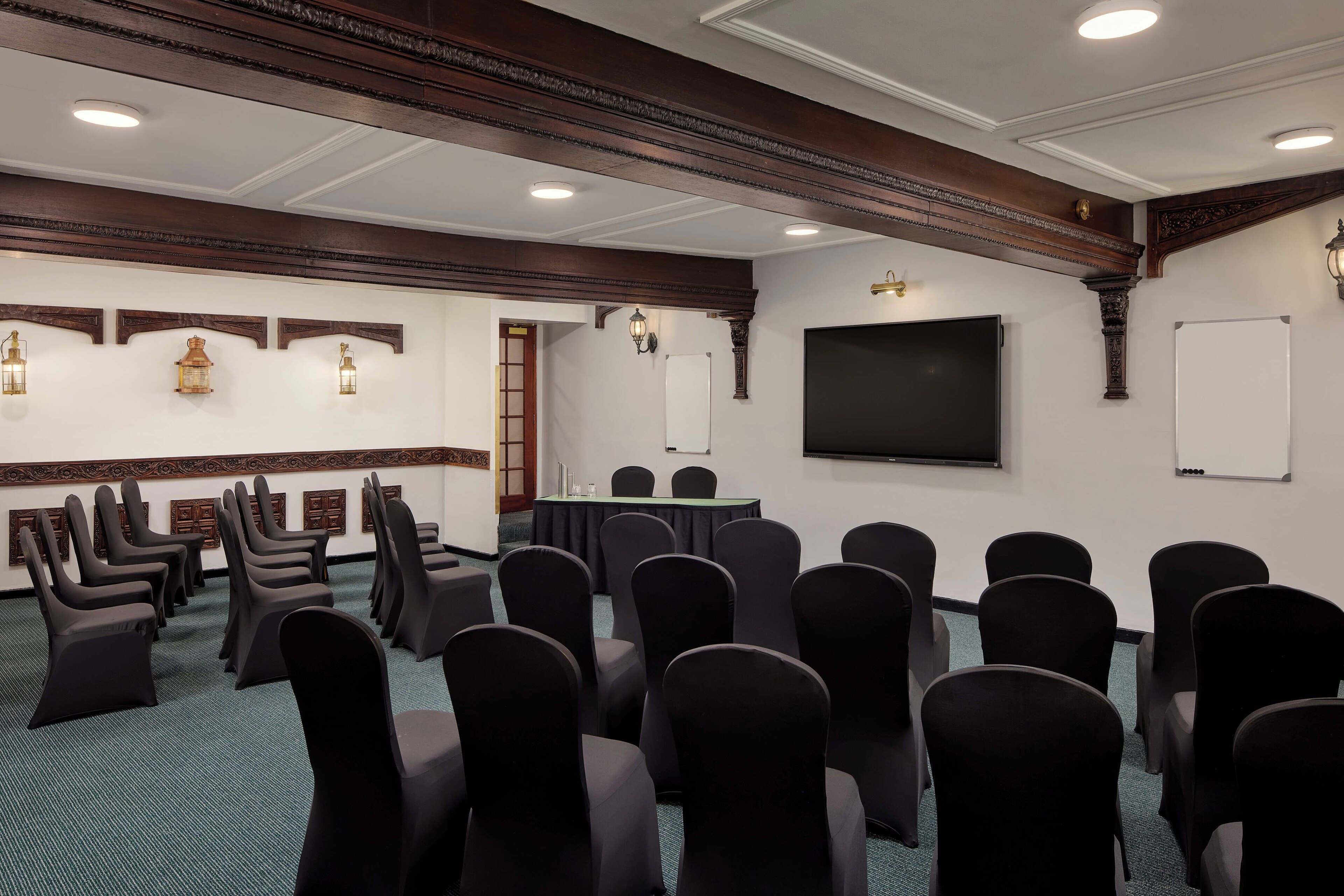A conference room with rows of chairs, a table, a screen, and decorative wall sconces.