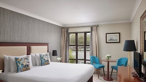Habitación de hotel con una cama grande, un escritorio, una silla, una lámpara y vistas a una masa de agua por la ventana.