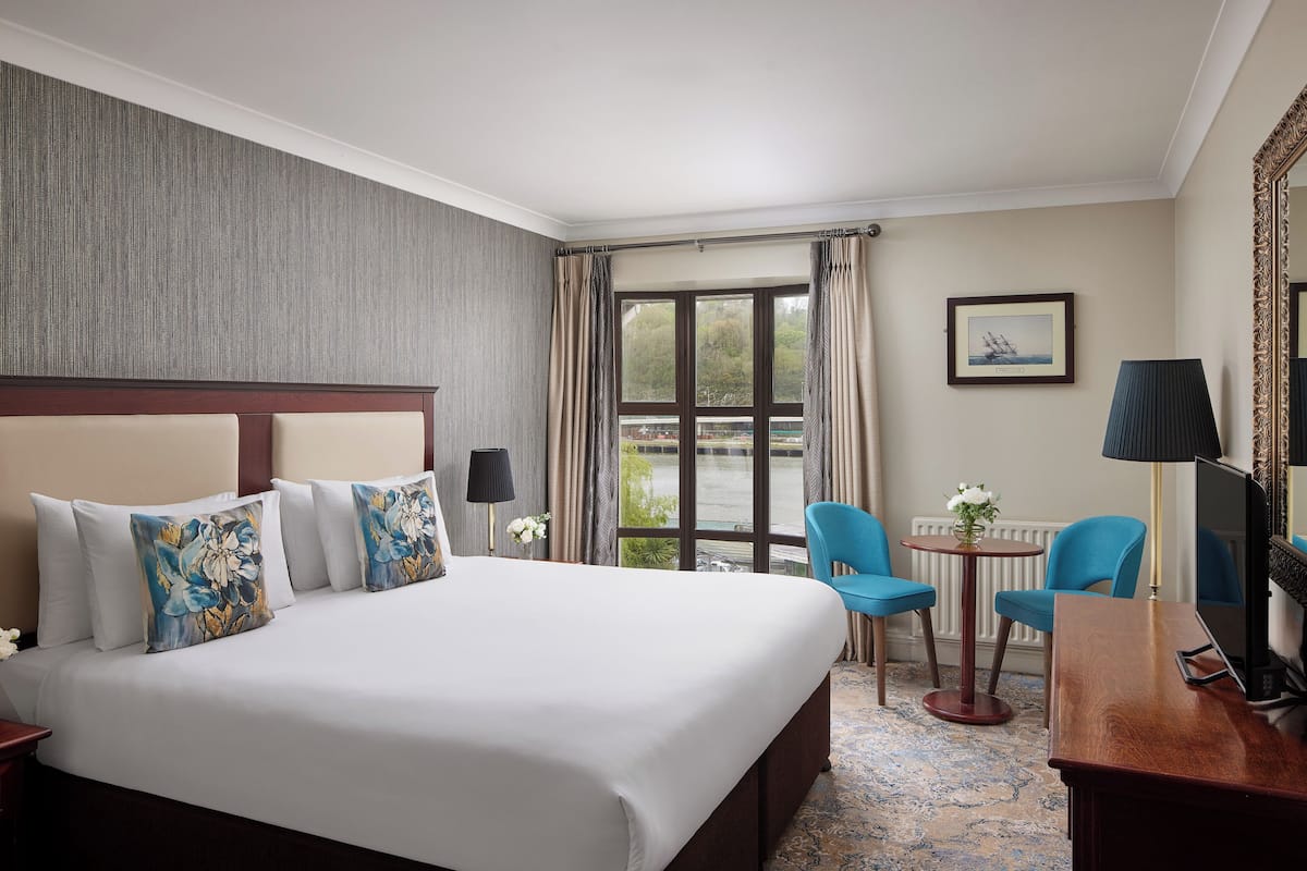 A hotel room with a large bed, a desk, a chair, a lamp, and a view of a body of water through the window.