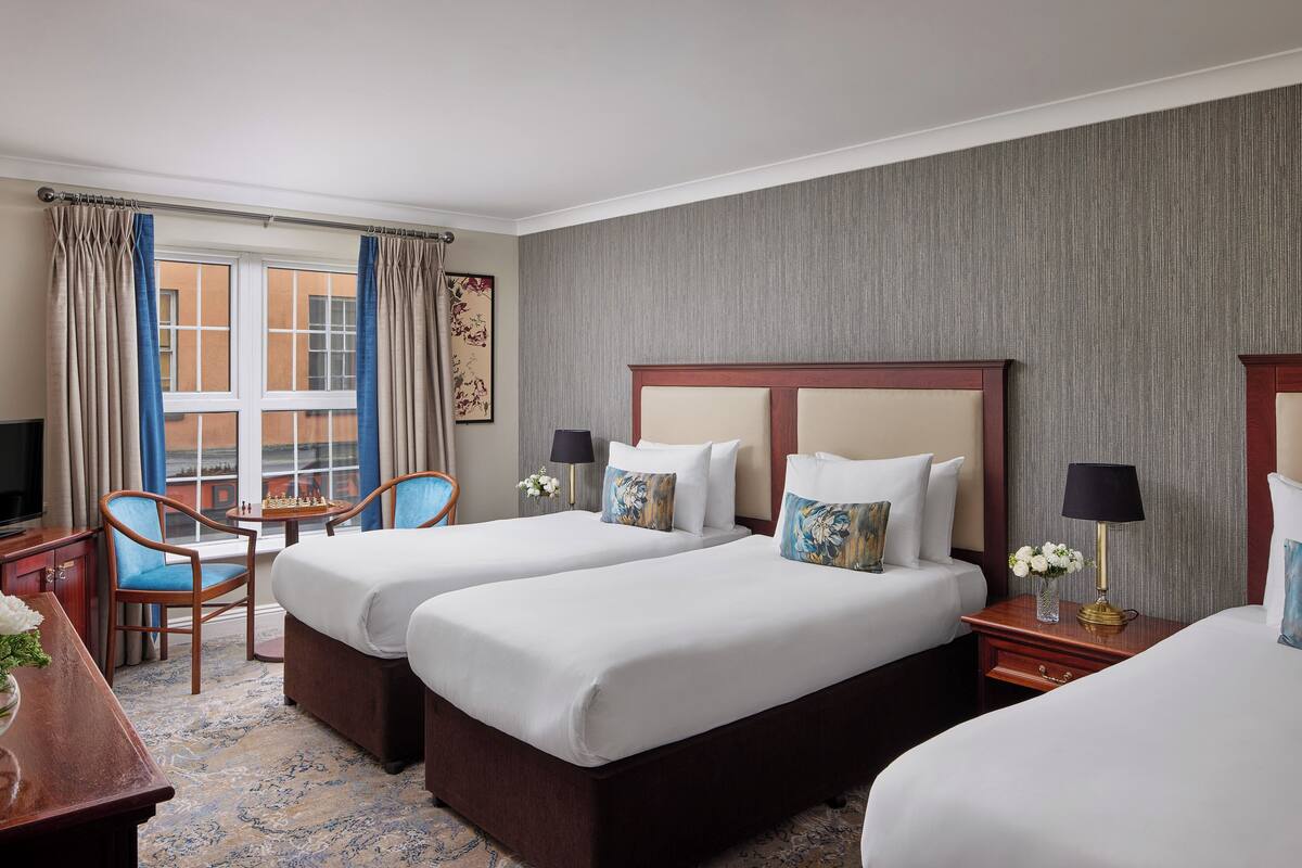 A hotel room with two beds, a desk, a chair, a lamp, and a window with curtains.