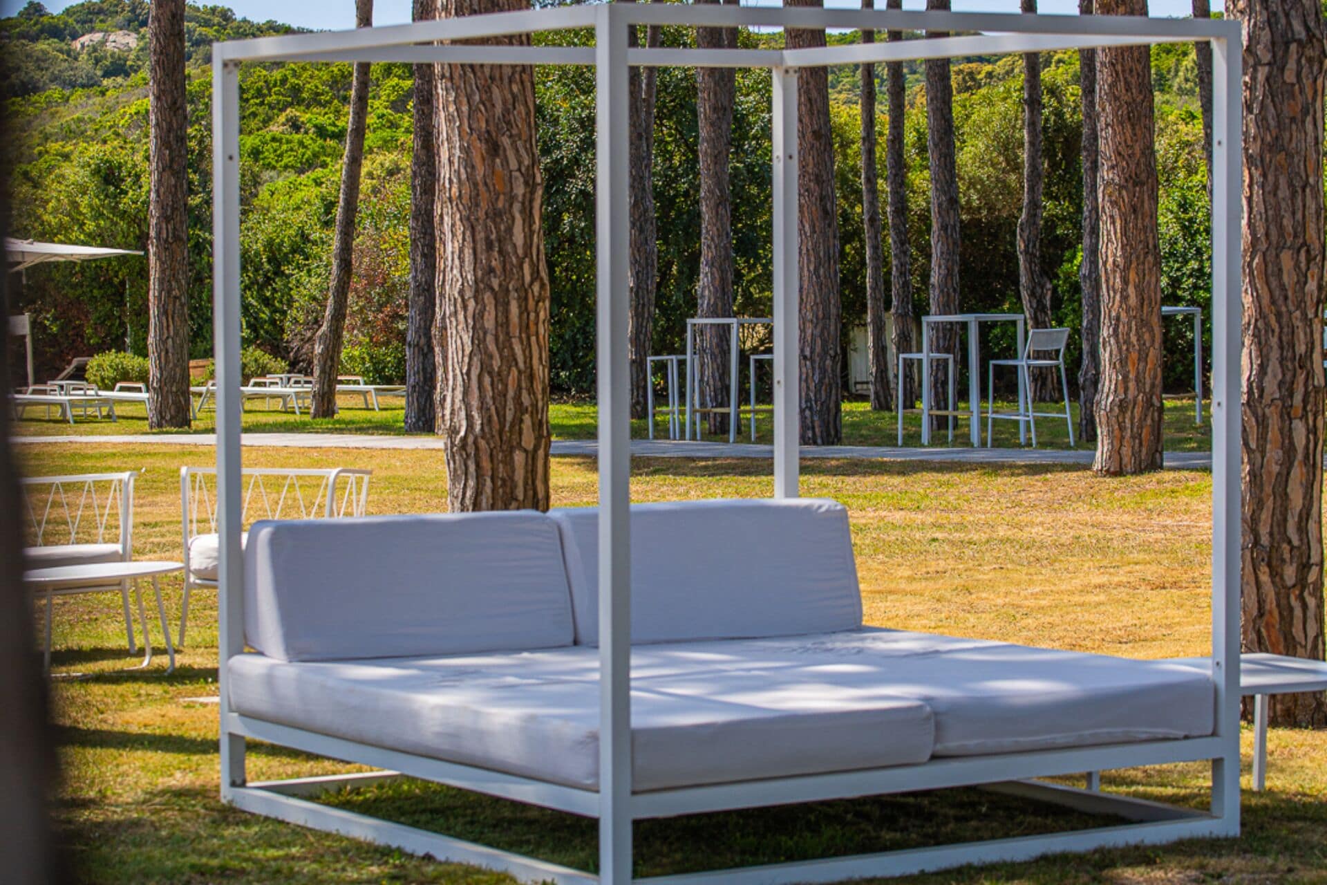 A white outdoor seating area with a metal frame, surrounded by trees.