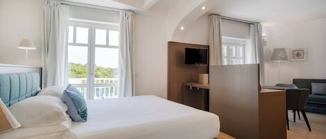 A modern hotel room with a large bed, a desk, a TV, and a balcony with curtains.