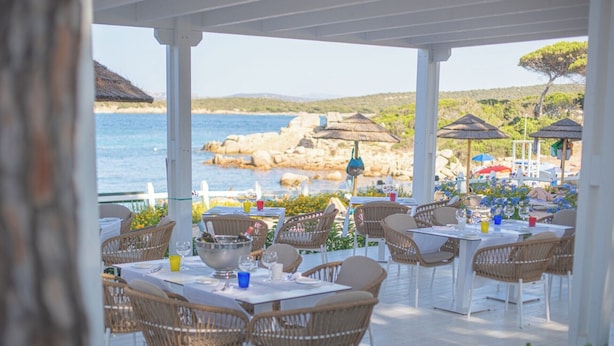 Un espace de restauration en plein air, avec des tables et des chaises en osier, offrant une vue sur une côte rocheuse.