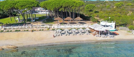 Un resort costero con aguas cristalinas, sombrillas de playa y vistas de las colinas circundantes.