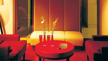 Una habitación de hotel moderna con un sofá, una mesa redonda con un florero y un ventanal con vistas.