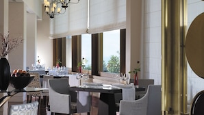 Un comedor amplio con techo alto, múltiples candelabros y ventanas grandes que ofrecen vistas al exterior.