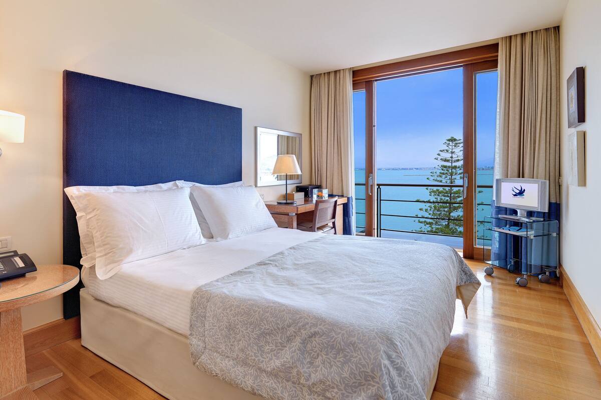 Habitación de hotel con una cama grande, un escritorio, una silla, un televisor y vista al mar.