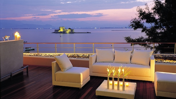 Terraza con dos sofás blancos y una mesita con velas, con vistas a una extensión de agua y una isla distante.