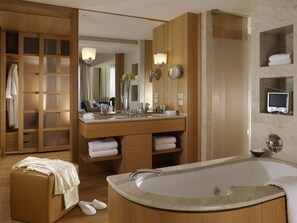 A modern bathroom with a large bathtub, wooden vanity, and a walk-in closet.