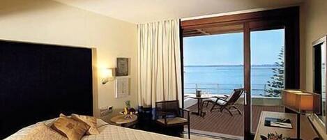 Habitación de hotel con cama, escritorio, silla y vista al mar a través de un ventanal grande.