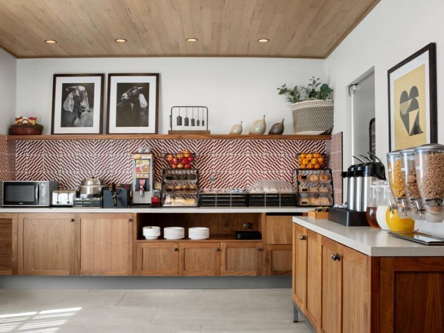 A modern kitchen with wooden cabinets, a microwave, a coffee machine, and various food items on the counter.