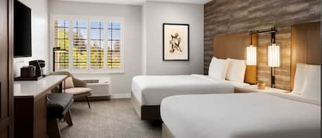A hotel room with two beds, a desk, a chair, a flat-screen TV, a framed artwork, and a window with blinds.