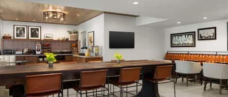 A modern kitchen with a large island, a dining area with a long table and chairs, and a seating area with orange chairs.