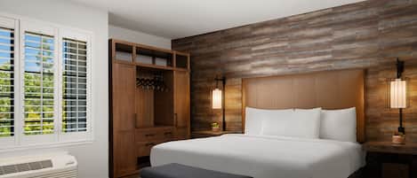 Ein Hotelzimmer mit einem großen Bett, einem Holzschrank, einer Bank, einem Heizgerät und einem Fenster mit Jalousien.