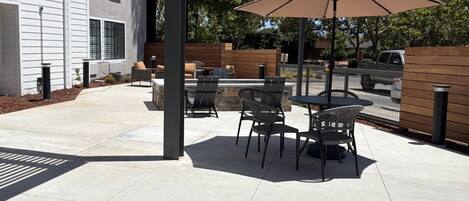 An outdoor patio with a table and chairs, a large umbrella, and a stone fireplace.