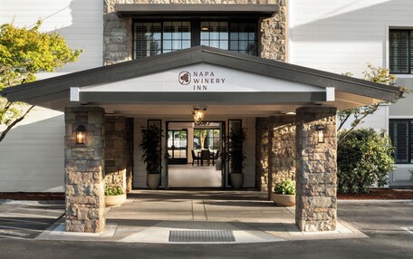 The entrance of Napa Winery Inn with stone pillars, a covered patio, and a sign above the entrance.