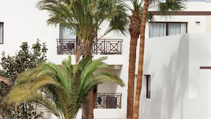 A courtyard with palm trees, a boat, and a thatched-roof structure. - Vitalclass Lanzarote Resort (Teguise)