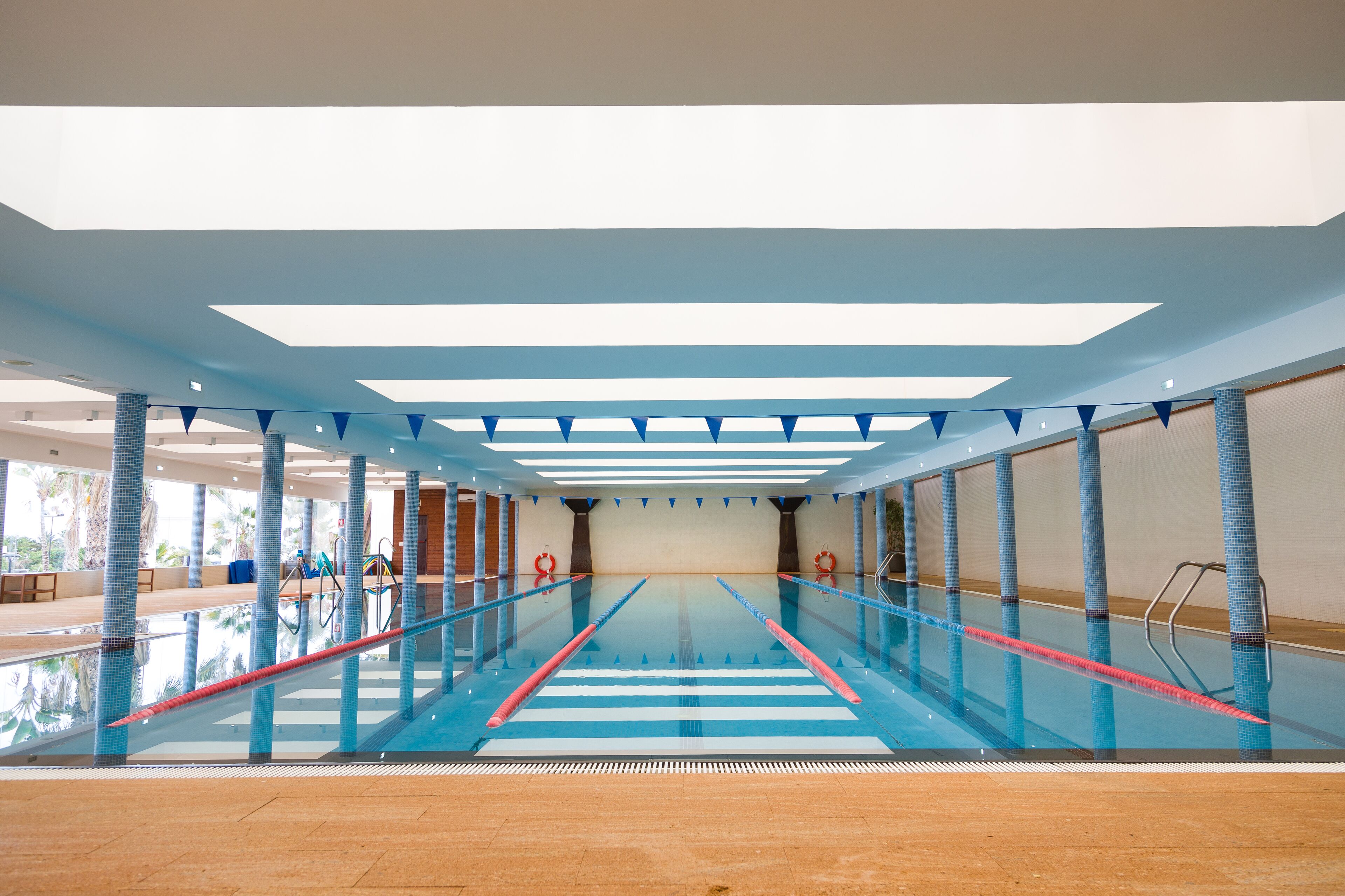 An indoor swimming pool with clear lanes, a tiled floor, and a ceiling with skylights.