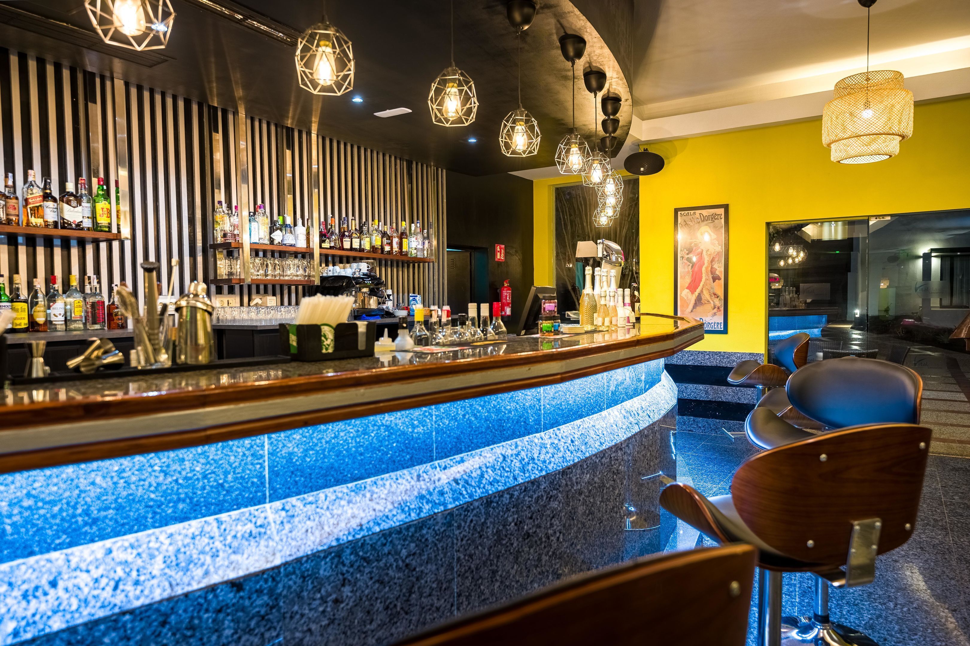 Un espace bar avec un comptoir aux carreaux bleus, des chaises en bois et des luminaires suspendus.