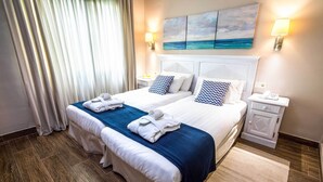 A hotel room with two beds, a large window with curtains, a painting of the ocean, and a bedside table with a lamp. - Vitalclass Lanzarote Resort (Teguise)