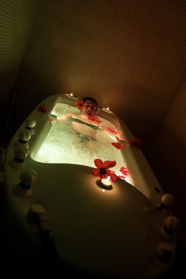 Une personne dans une baignoire remplie d’eau, entourée de fleurs et de bougies.