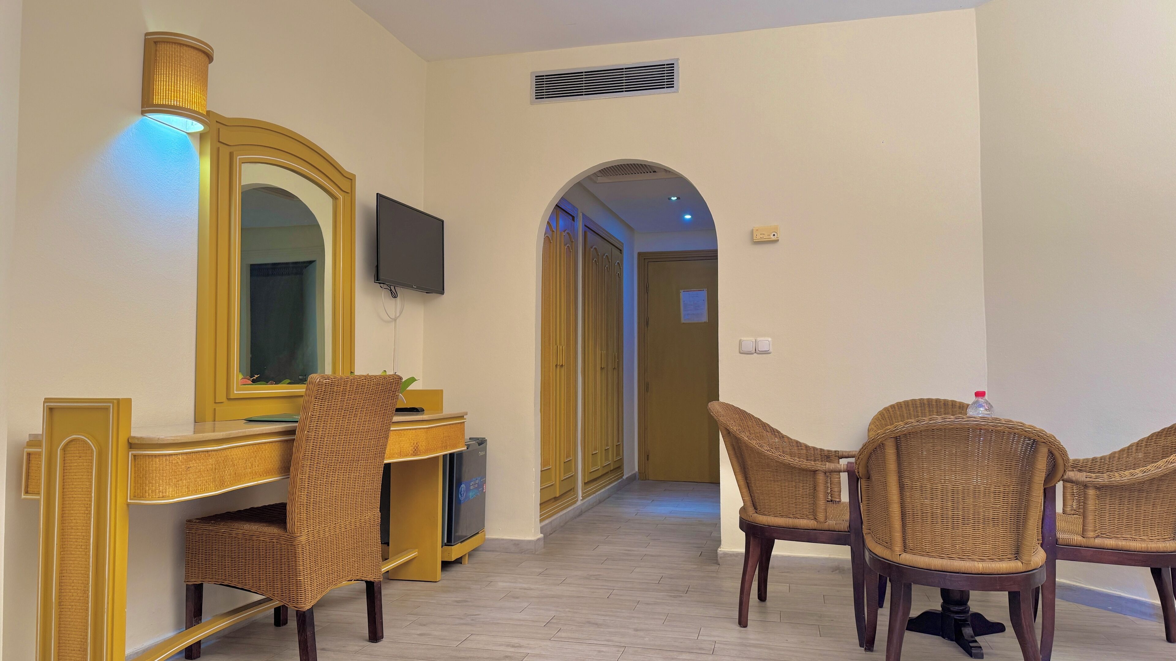 A hotel room with a desk, chairs, a television, and a mirror.