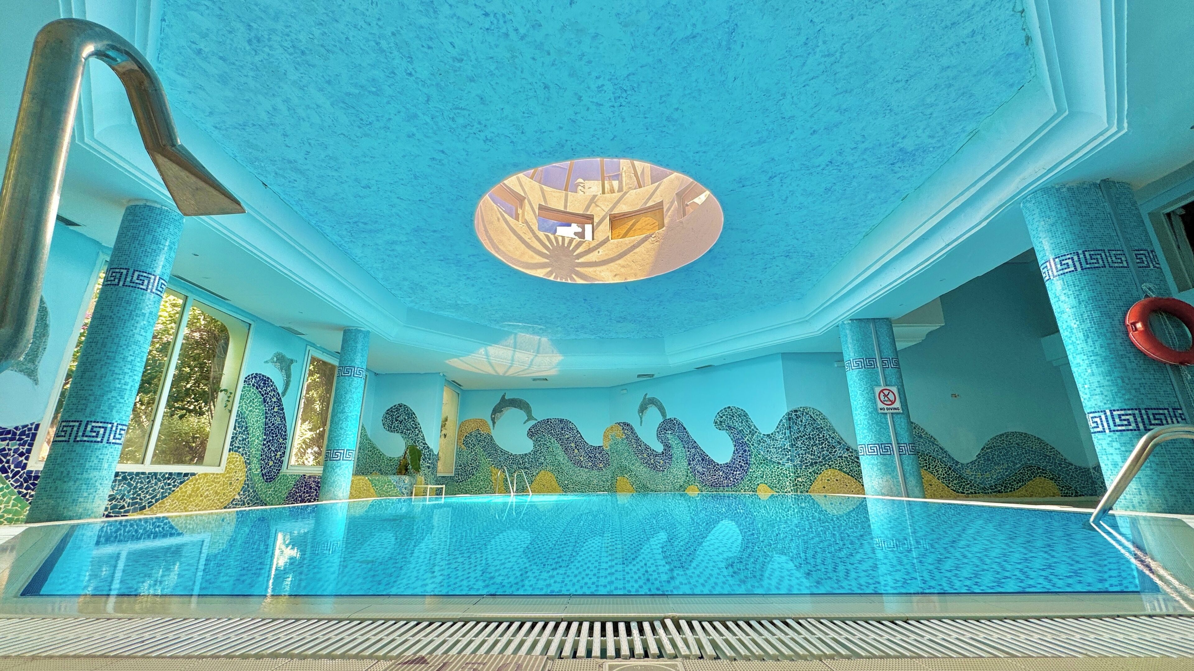 A swimming pool with mosaic tile walls and a circular skylight.