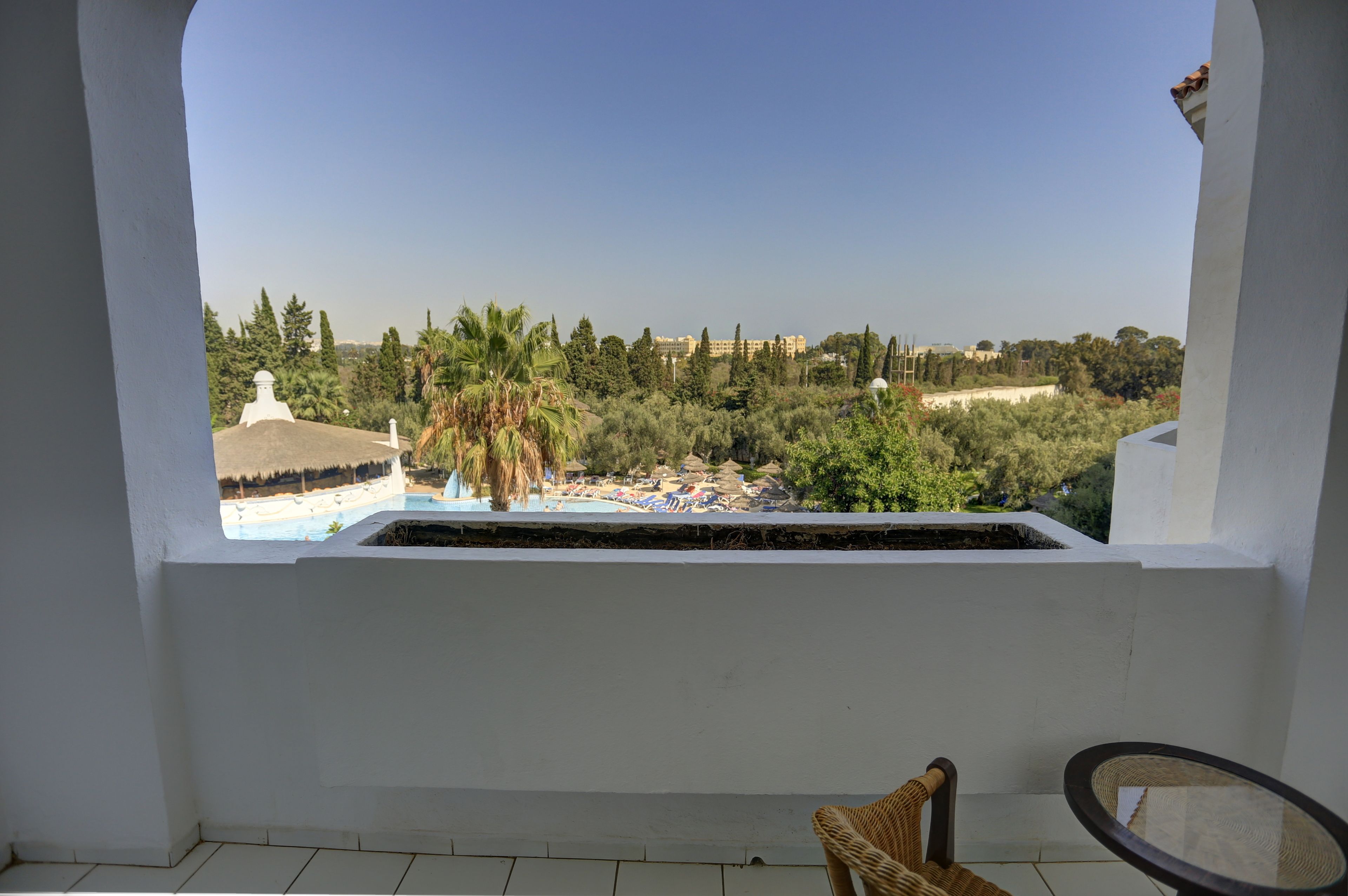 Un balcon avec vue sur une piscine, des palmiers et un bâtiment situé au loin.