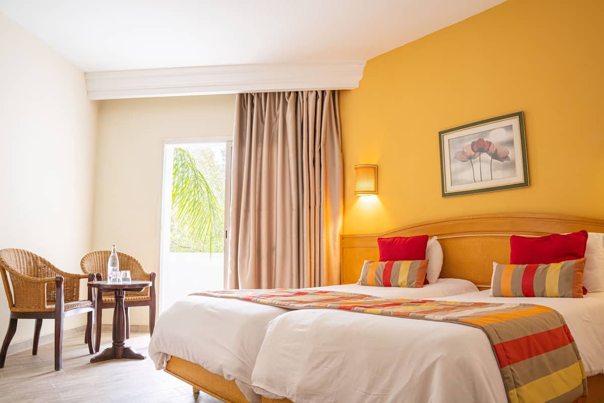 Une chambre d’hôtel avec un lit, une chaise, une table et une fenêtre avec des rideaux.