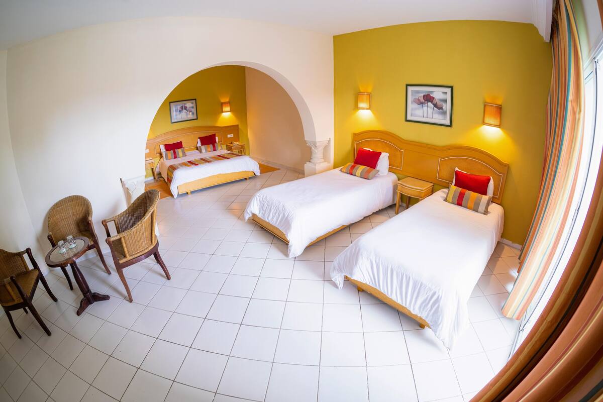 Une chambre d’hôtel avec trois lits, une table à manger avec des chaises et un petit coin salon.