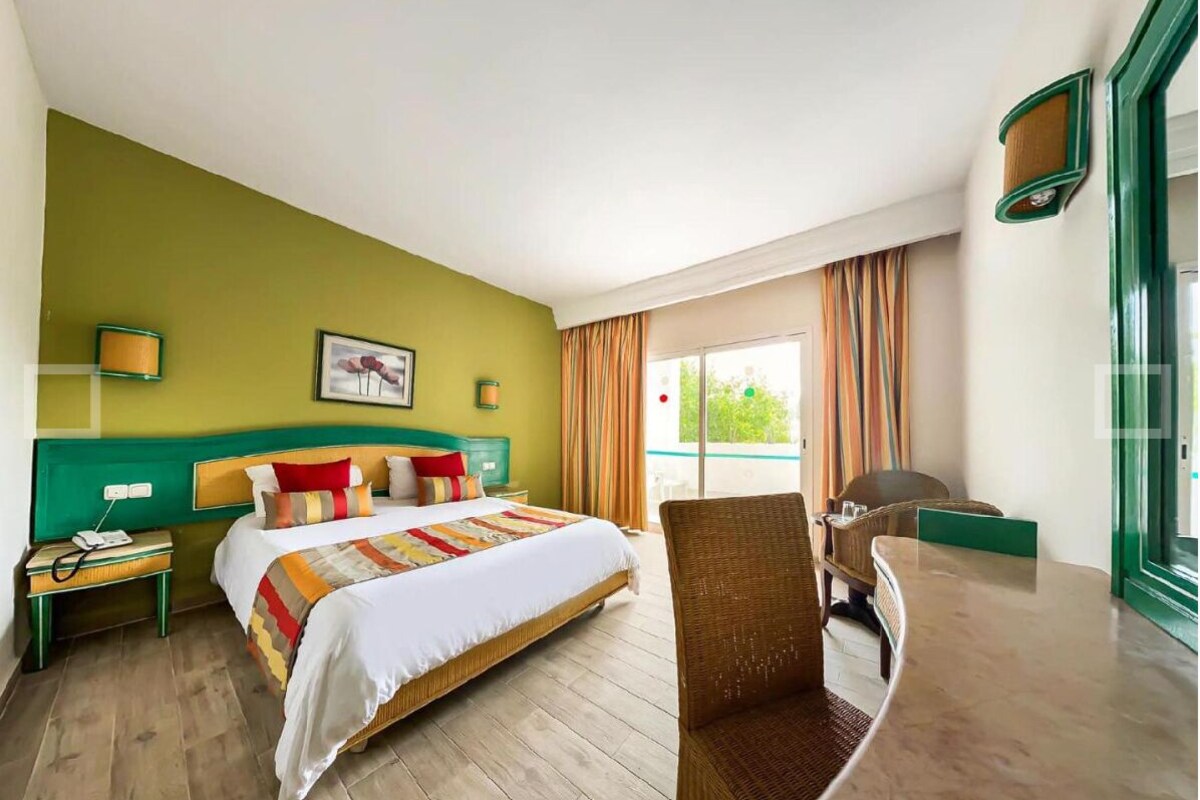 Habitación de hotel con una cama grande, una silla, un escritorio con lámpara y vistas al exterior.