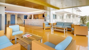 Eine geräumige Lobby mit einer Rezeption, einer Sitzecke mit Sofas und Sesseln sowie einer Treppe zu einer oberen Etage.