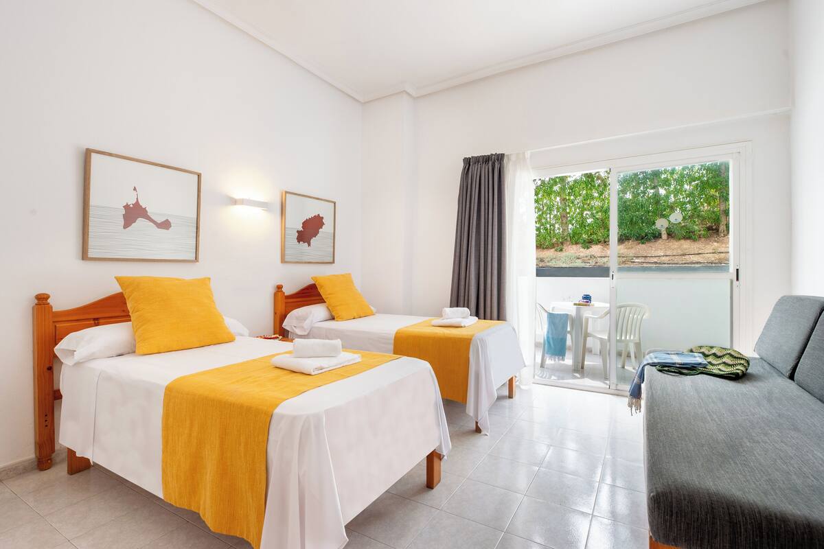 Une chambre d’hôtel avec deux lits, un canapé, un balcon et un coin repas.