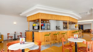 Un espace bar avec des tabourets et des tables en bois, un comptoir où sont servis les boissons, et un coin salon avec des chaises.