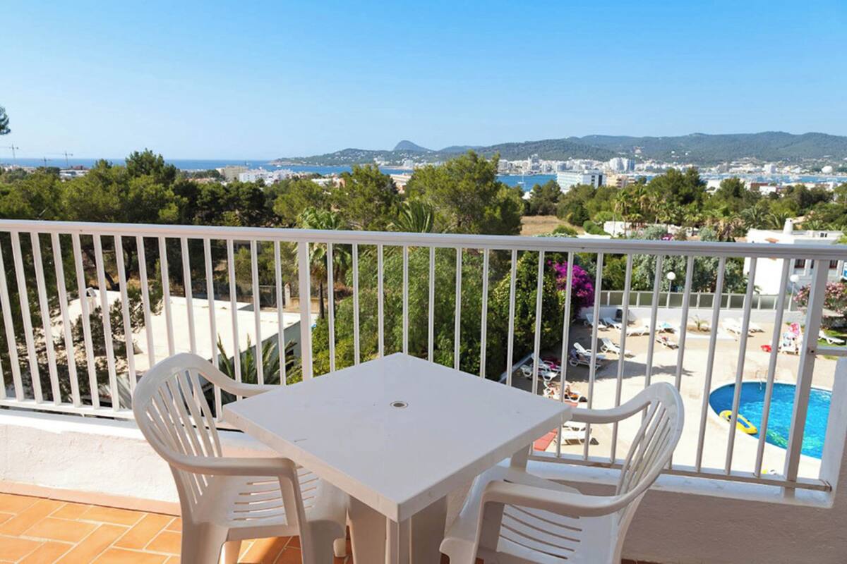 Un balcon avec une table et des chaises blanches, donnant sur une piscine et offrant une vue sur la côte.