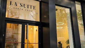 L’extérieur de l’hôtel La Suite Santa Cruz, avec ses grandes portes vitrées et sa façade moderne.