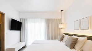 Une chambre d’hôtel avec un grand lit, un banc, un téléviseur à écran plat et une fenêtre avec des rideaux légers.