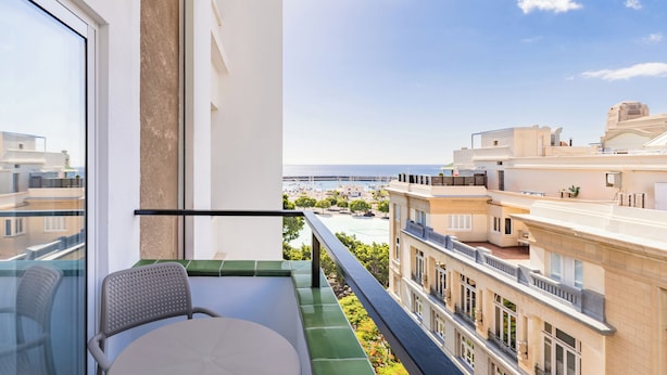 Un balcon avec une chaise et une table, donnant sur un paysage urbain avec des bâtiments et un ciel dégagé.