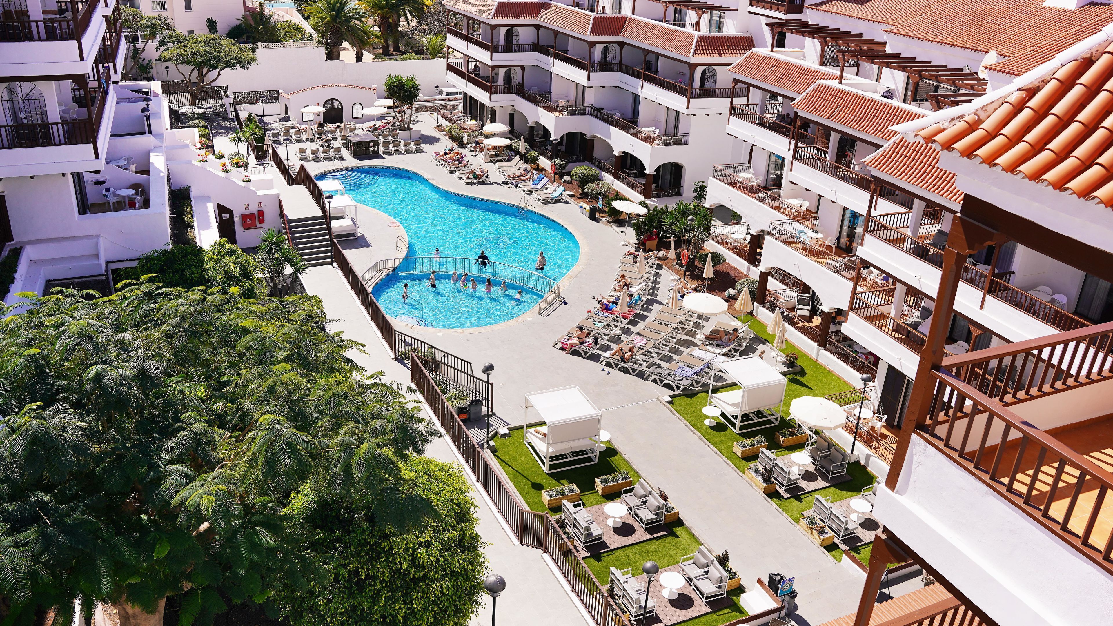 A hotel with a swimming pool, outdoor seating, and multiple balconies.
